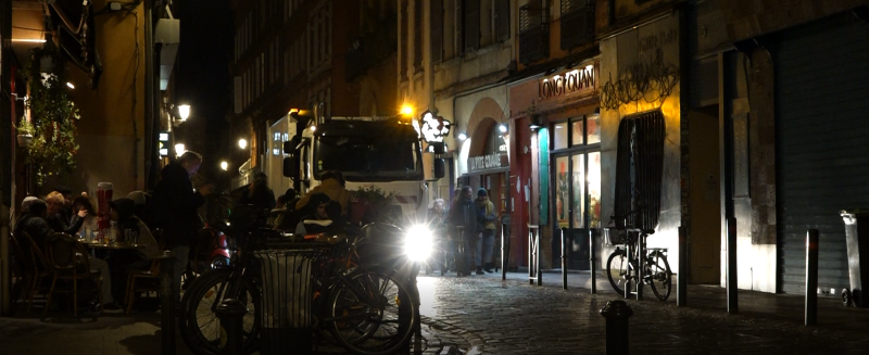 Le camion-benne des éboueurs longe les terrasses des bars de la rue Peyrolières à Toulouse. 